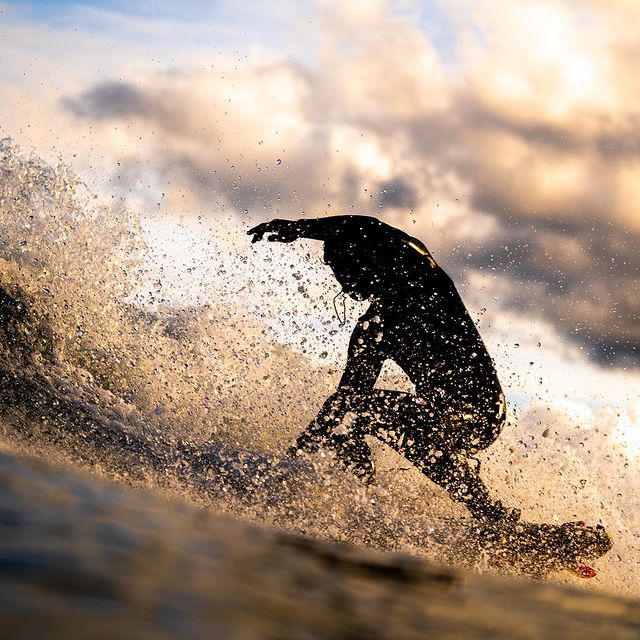 Silhouette of a surfer midway through a turn on a crisp wave with fluffy clouds as a backdrop