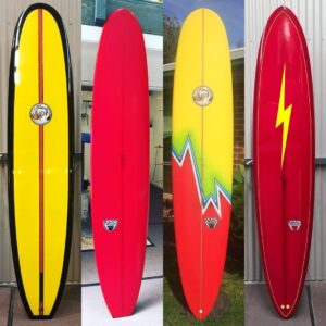 Four longboards created by NMC Surfboards in red and yellow with gloss finish and Aboriginal flag and Lightning Bolt inspired artwork